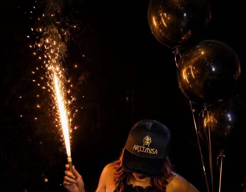 Cumpleañera con gorra de Artemisa y una bengala encendida, junto a globos negros